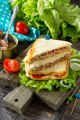 Double sandwich with canned tuna and feta cheese served with lettuce leaves on a wooden cutting board.