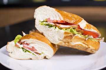 Fresh sandwich with ham, cheese, bacon, tomatoes, lettuce, cucumbers and onions on dark wooden background. Delicious restaurant meal.