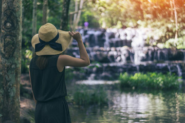 Young woman traveler and freedom. Young woman in hat with rucksack enjoying tropical waterfall view.