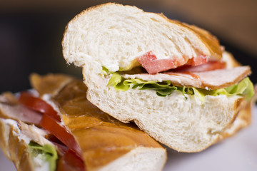 Fresh sandwich with ham, cheese, bacon, tomatoes, lettuce, cucumbers and onions on dark wooden background. Delicious restaurant meal.