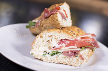 Fresh sandwich with ham, cheese, bacon, tomatoes, lettuce, cucumbers and onions on dark wooden background. Delicious restaurant meal.