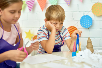 Portrait of sad little boy refusing to work in art and craft class of development school while...