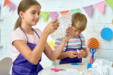 Portrait of pretty girl holding paper snowflake while making handmade Christmas decorations during art and craft class of pre-school