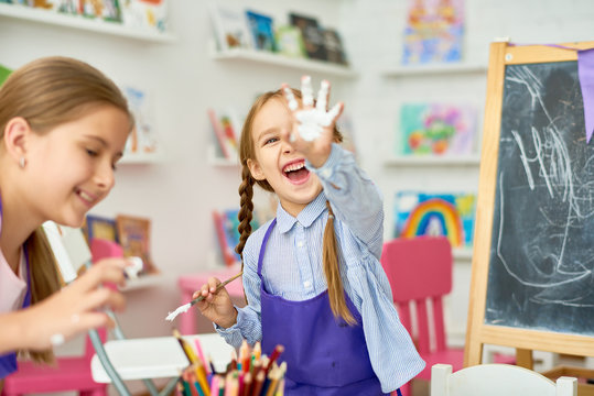 Portrait of two little girls enjoying art and craft lesson in development school and smiling happily to camera showing  hands in paint