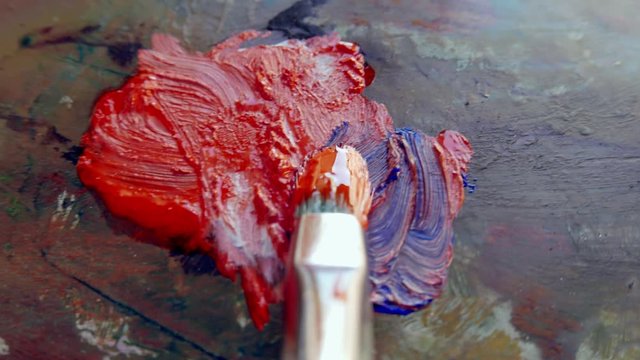 a paintbrush mixing red and blue paint on a palette