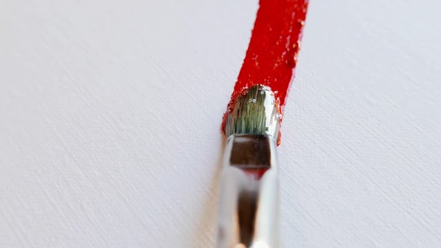 a paintbrush mixing red and blue paint on a palette