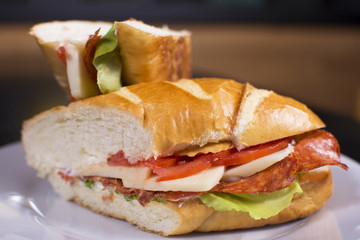 Fresh sandwich with ham, cheese, bacon, tomatoes, lettuce, cucumbers and onions on dark wooden background. Delicious restaurant meal.