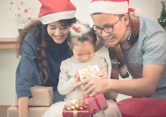 Happy family Asia family wear santa claus hat unwrap Christmas gift box at house xmas party,Holiday celebrating festive concept,vintage filter.