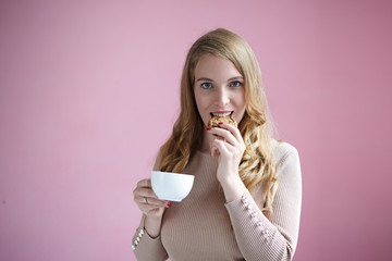 Charming young Caucasian female in casual clothes enjoying delicious homemade cookie and coffee. Portrait of pretty woman eating raisin biscuit and drinking tea for breakfast before going to work - obrazy, fototapety, plakaty