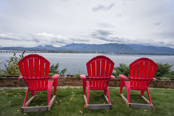 Three red lawn chairs by the lake.