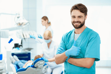 A dentist poses against the backdrop of a dental office. He show thumbs up