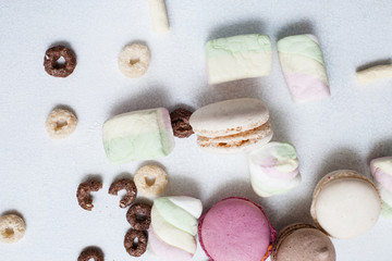 Colorful sweets on white background top view. Delicious macaroons, marshmallow and corn flakes are spread around, close up