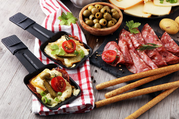Delicious traditional Swiss melted raclette cheese on diced boiled or baked potato served in individual skillets with salami..