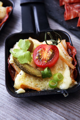 Delicious traditional Swiss melted raclette cheese on diced boiled or baked potato served in individual skillets with salami..
