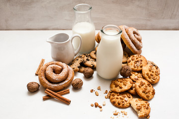 Culinary background of home-baked shop. Wholegrain scones, baked rolls,walnuts and spices laying near bottles of milk on white table. Concept of delicious rustic breakfast with cookies