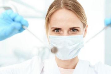 A dentist in a white medical mask is holding a dental mirror and a probe