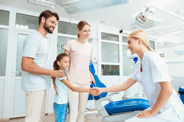 Fototapeta premium A girl at a dentist's reception. She smiles and talks to the doctor. Next to her parents