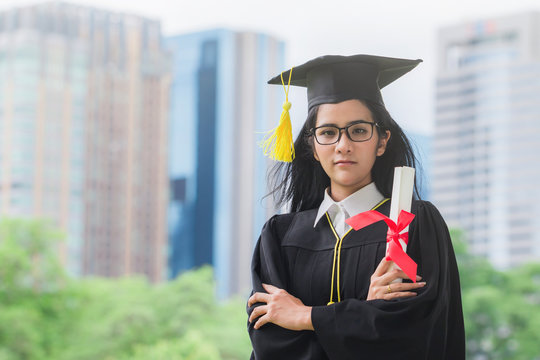 Happy graduate young Asian woman in cap and gown holding certificated in hand, Education concept