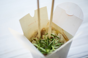 Noodles with pork and vegetables in take-out box on wooden table