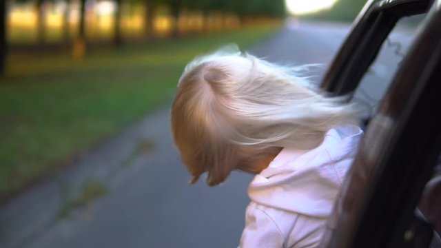 Kid with hair in the wind riding in the car.