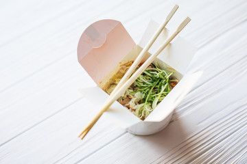 Chinese noodles in takeaway box on wooden background. Food.