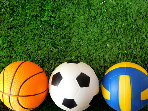 Balls for soccer, basketball and volleyball are lying on the green grass. Different sports concept