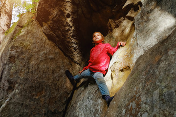 Small boy climbing on the rocks in the forest
