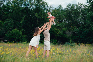 young happy family with little beautiful baby with blue eyes walking in summer park at sunset.