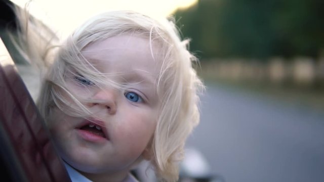 Kid with hair in the wind riding in the car.