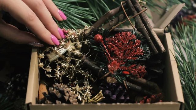 Festive box with decoration. Close up handmade wooden house, golden garland, strobilas and red felt fir tree gathering in carton. New Year and Christmas traditions and decor concept