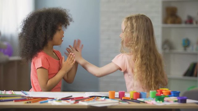 Positive Afro-American and Caucasian girls clapping hands, happy childhood