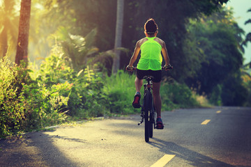 Young  woman cycling on tropical forest trail