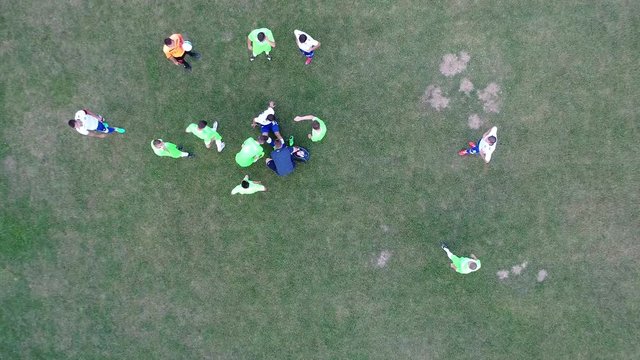 Injuried soccer player laying on ground while medical support staff helping. Team players waiting and resting . Aerial flat lay flaying above top view  footbal game break