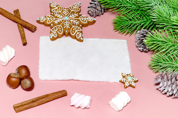 Christmas greeting card over wooden light pink table with snow fir tree, snowflakes, nuts, marshmallow and cinnamon. Flat lay slyle