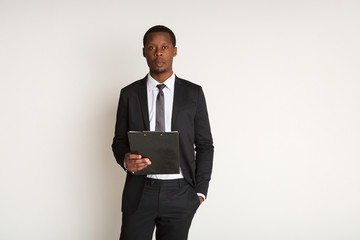 Black male pensive manager in suit standing, holding laptop. Portrait