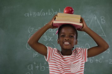 Schoolgirl holding books stack with apple on head against