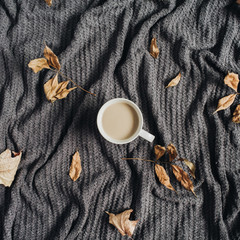 Coffee with milk and dry fall autumn leaves on warm grey plaid. Autumn flat lay.