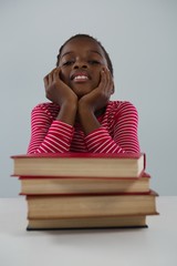 Schoolgirl relaxing in front of books stack against white