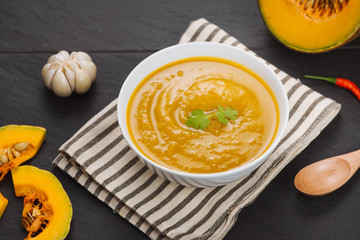 Bowl of pumpkin soup on black stone background.