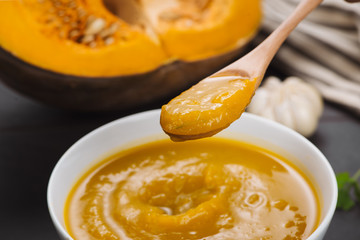 Spoon of homemade pumpkin soup on blank stone background.