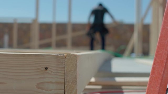 Wood Framing Close Up with Worker. view moves right on a close up on the end of a framed wall on the construction site with a construction worker in the background
