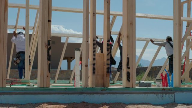 Construction Workers Lift Framed Wall Into Place. view moves right as construction workers lift a framed wall into place for residential home construction
