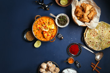 Indian cuisine on diwali holiday: tikka masala, samosa, patties and sweets with mint chutney and spices. Dark blue background, copy space. Diwali celebration dinner