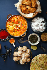 Indian cuisine on diwali holiday: tikka masala, samosa, patties and sweets with mint chutney and spices. Dark blue background. Vertical composition