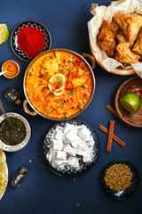 Indian cuisine on diwali holiday: tikka masala, samosa, patties and sweets with mint chutney and spices. Dark blue background. Vertical composition. Diwali celebration dinner