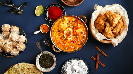 Indian cuisine on diwali holiday: tikka masala, samosa, patties and sweets with mint chutney and spices. Dark blue background. Banner composition