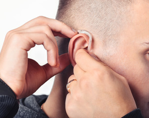 Fototapeta premium Young man hearing impaired dressing the hearing aid. At isolated white background.