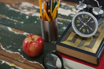 Alarm on stack of books with pen holder, apple, and magnifying