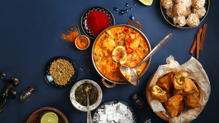 Indian cuisine on diwali holiday: tikka masala, samosa, patties and sweets with mint chutney and spices. Dark blue background. Banner composition. Diwali celebration dinner