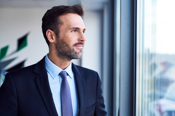 Fototapeta premium Smiling businessman standing in office and looking through window